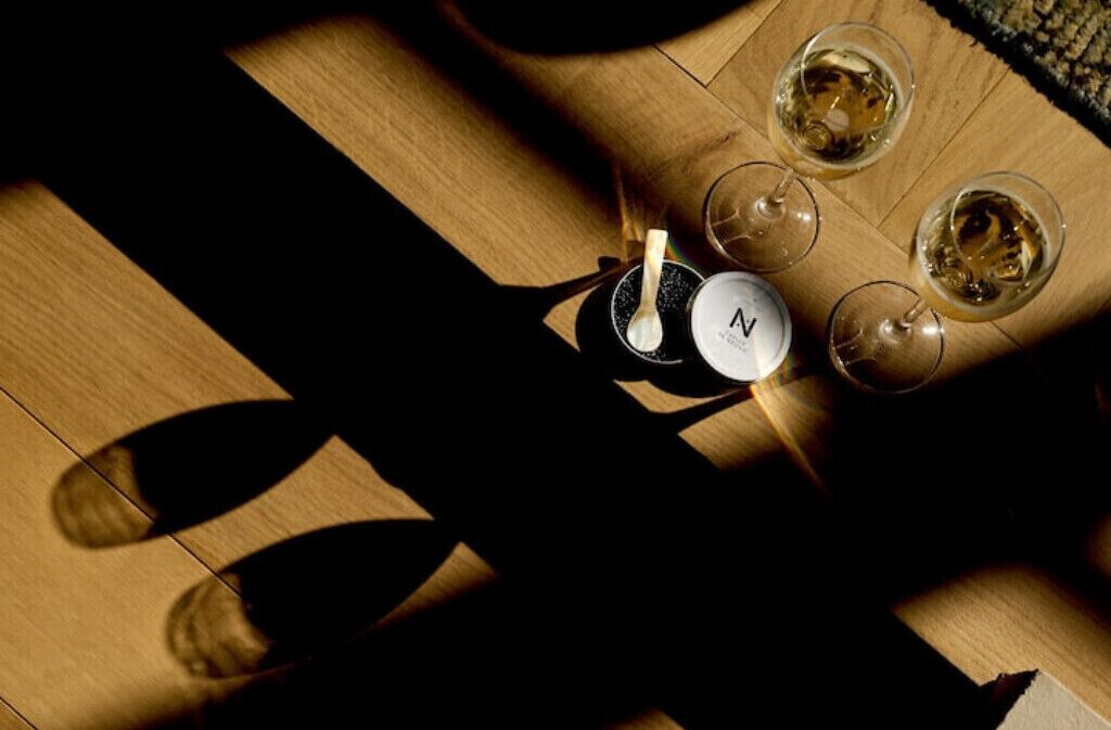 A wooden floor with four glasses of white wine and a bottle with a spoon.