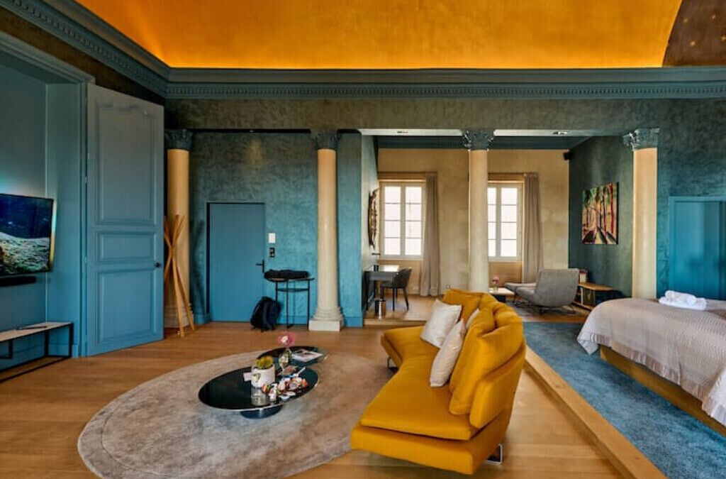 Een ruime kamer met een gele bank, een bed en een eethoek.