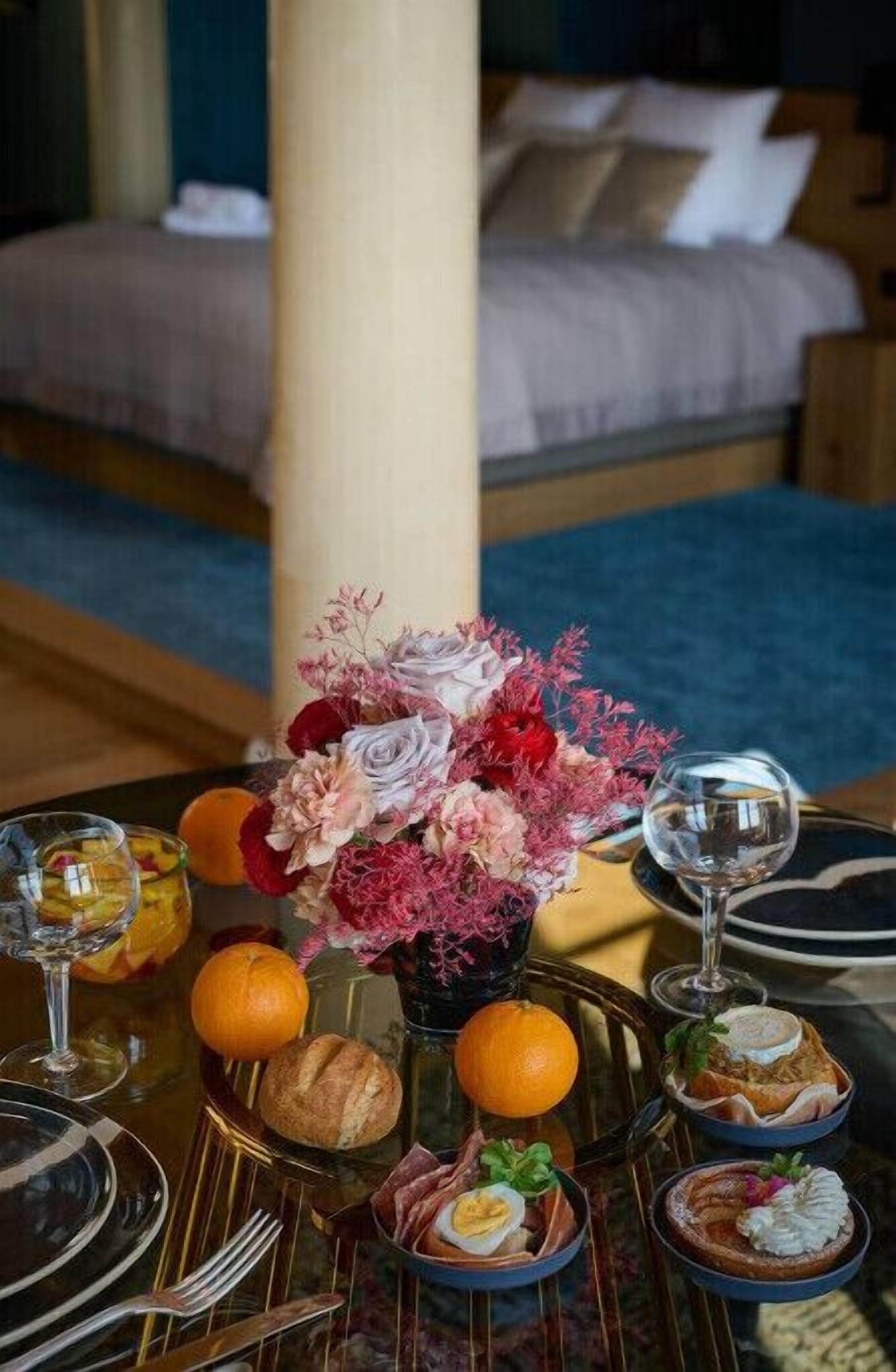 Een eettafel gedekt met een bloemstuk, borden, bestek, glazen en diverse soorten eten.