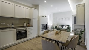 A modern kitchen with white cabinets, a built-in oven, and a dining area with a wooden table and chairs. - Il Nespolo Charming Apartment Fonterutoli (Castellina in Chianti)
