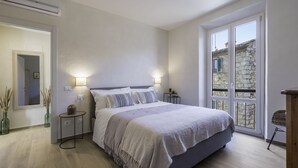 A bedroom with a large bed, bedside lamps, a small table, and a view through a window. - Il Nespolo Charming Apartment Fonterutoli (Castellina in Chianti)