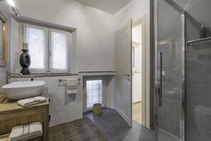 Un baño moderno con un lavamanos tipo recipiente, una cabina de ducha de vidrio y una pequeña ventana con vidrio esmerilado.