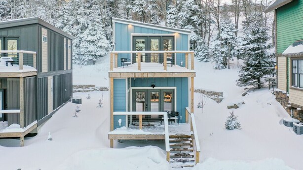 Una cabaña de dos pisos con balcón, rodeada de árboles nevados.