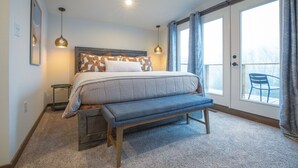 Un dormitorio con cama, banca, mesitas de noche y vistas al exterior a través de un ventanal corredera.