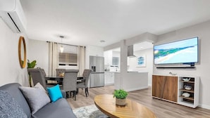 A modern living room with a sofa, dining table, and kitchen in the background. - Ultimate Oceanside Retreat | Tower 9 Across from the Beach (Oceanside)