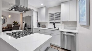 A modern kitchen with white cabinetry, stainless steel appliances, and a central island. - Ultimate Oceanside Retreat | Tower 9 Across from the Beach (Oceanside)
