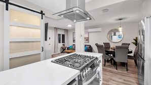 A modern kitchen with a central island, a dining area with a round table, and a large mirror on the wall. - Ultimate Oceanside Retreat | Tower 9 Across from the Beach (Oceanside)