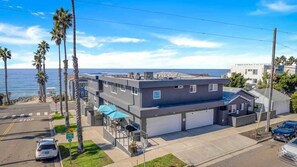 Situated on a coastal street, this two-story residence offers a garage and a patio area with outdoor seating.