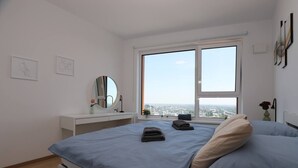 Un dormitorio moderno con una cama grande, una mesita de noche, un espejo y una ventana con vista a la ciudad.