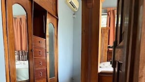 A room with a wooden wardrobe, a tiled floor, and an air conditioning unit on the wall.