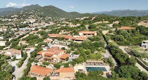 An aerial view of a residential area with houses, a swimming pool, and a mountainous backdrop.