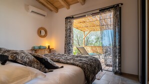 A bedroom with a bed, a nightstand, a lamp, and a view of an outdoor patio with a chair and umbrella. - Résidence U Frusteru (Propriano)