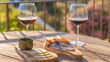 A wooden table with two glasses of red wine, a small bowl, and a wooden board with sliced cheese and cured meats.
