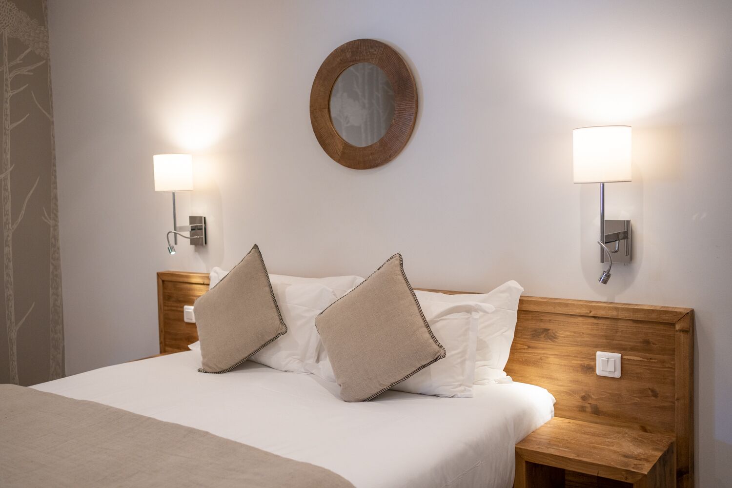 Een opgemaakt bed met twee kussens, een ronde spiegel aan de muur en twee wandlampen.
