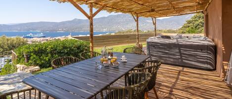 Un patio exterior con una mesa lista para el desayuno, un jacuzzi y una vista panorámica del mar y las montañas.