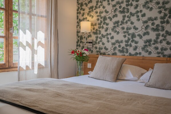 A neatly made bed with a wooden headboard, a vase with flowers, and a wall with a pine tree pattern.