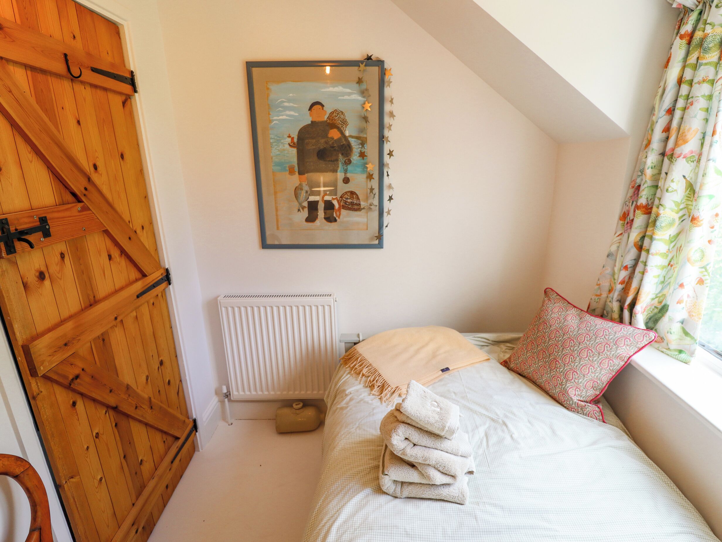 A bedroom with a wooden door, a radiator, a bed with a patterned pillow, and a framed artwork on the wall.