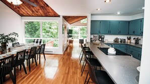 A modern kitchen with wooden flooring, a large island, and teal cabinets. - Riverfront FirePit! HotTub-Pool-Beaches-Gameroom (Gouldsboro)