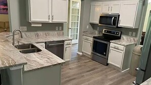 Una cocina con armarios blancos, un lavaplatos de acero inoxidable, un microondas y una estufa.