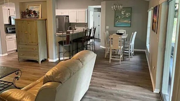 Un salón amplio con un sofá beige grande, una zona de comedor con mesa y sillas, y una cocina al fondo.