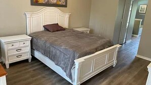 Un dormitorio con cama, mesitas de noche, cómoda y un cuadro en la pared.