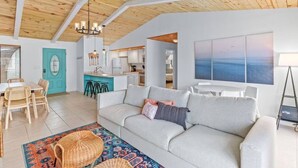 A spacious living area with a high ceiling, a sofa, a dining table with chairs, and a kitchen in the background. - New! Big Discounts!! Nights of Lights, Beach, Cowboy Pool, Bike, Grills, Pets (St. Augustine)