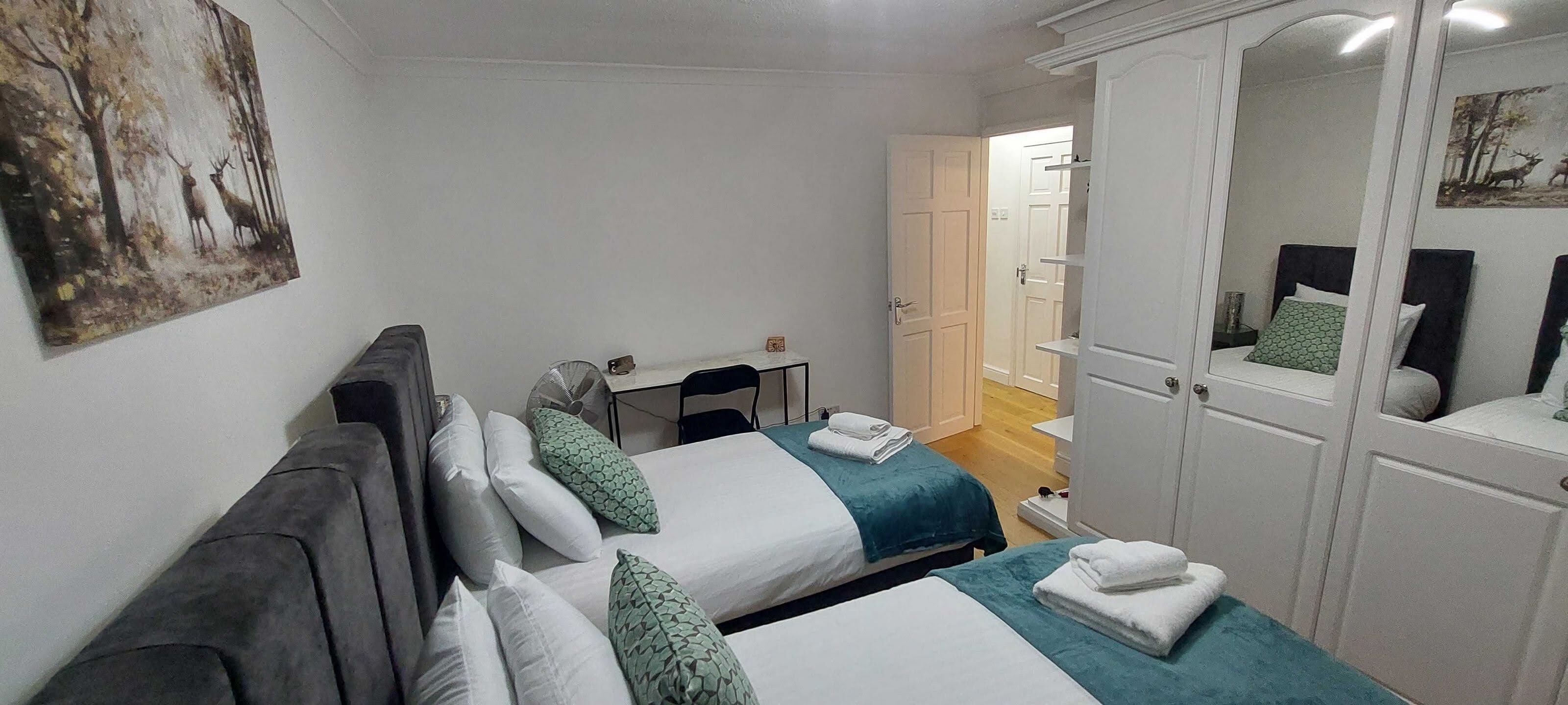 A hotel room with two beds, a desk, a chair, and a wardrobe.