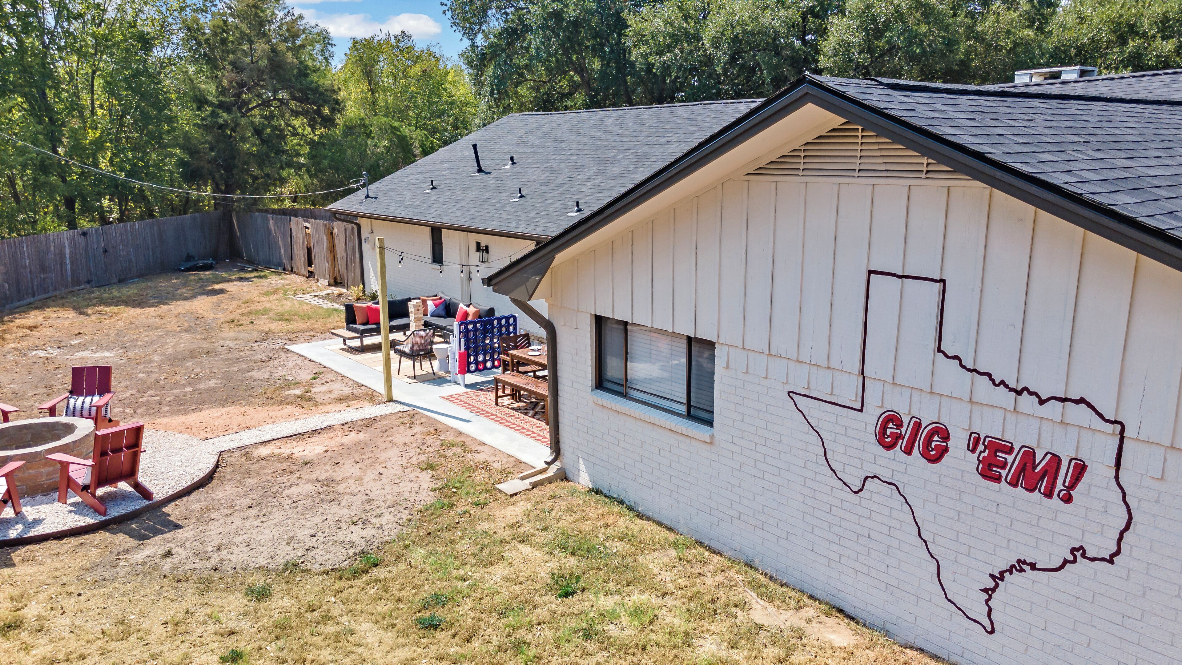 Una casa con fachada blanca, un patio con mobiliario exterior y un letrero que dice 'GIG 'EM!' en el lateral.
