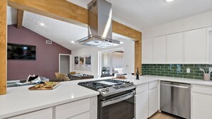 Una cuina moderna amb armaris blancs, un fogó d'acer inoxidable i un forn integrat.