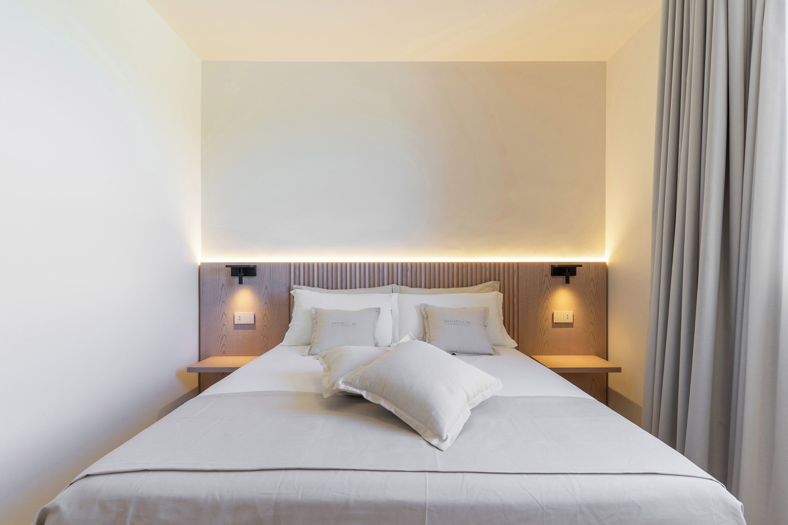 A neatly made bed with white linens, two bedside tables with lamps, and a headboard with integrated lighting.