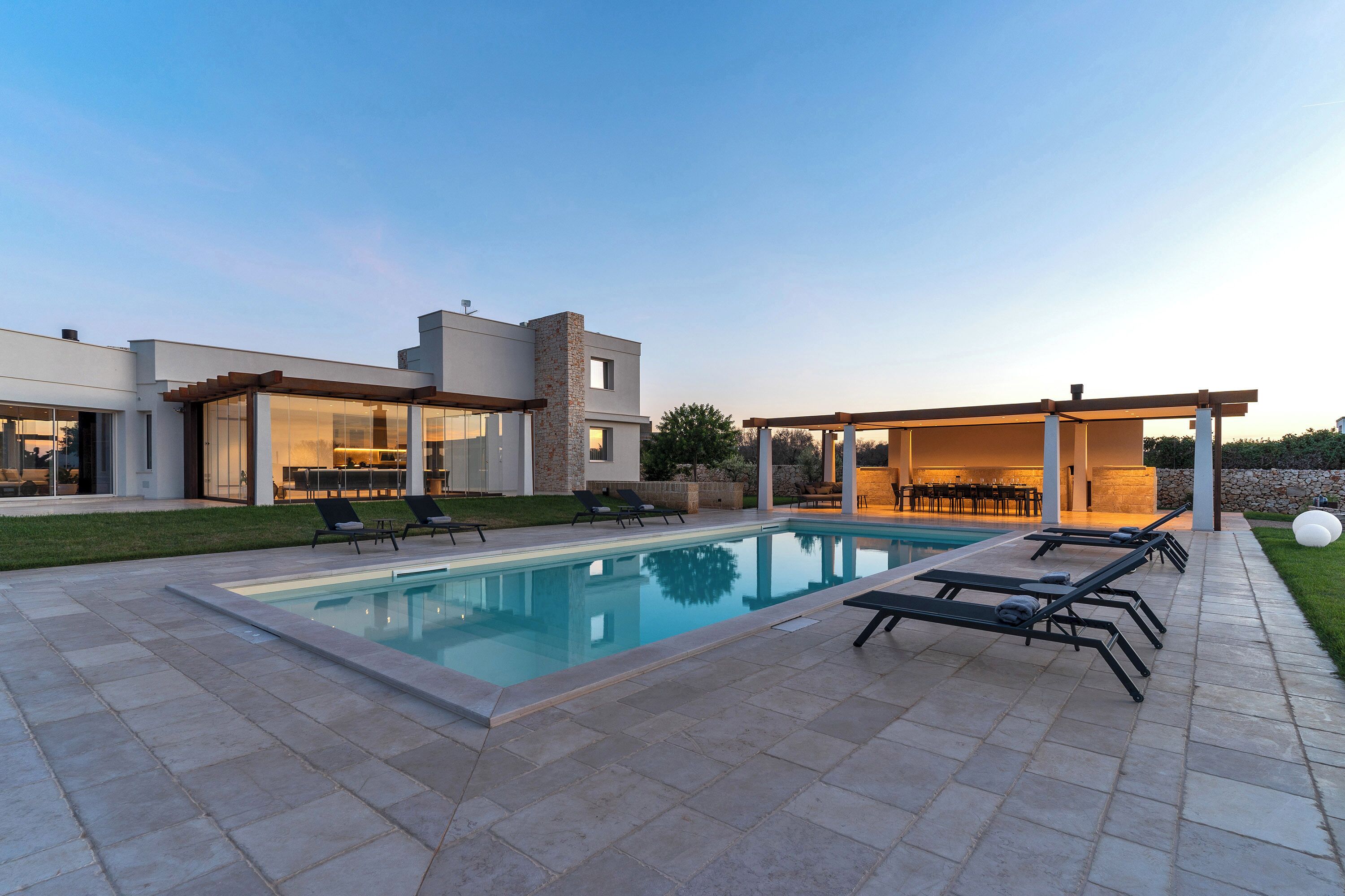 Una casa moderna con piscina, area salotto esterna e patio.