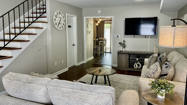 A living room with a staircase, a clock, a TV, a sofa, a coffee table, and a lamp. - Modern Townhome w/ Balcony • Walk to FUSE Stadium (Gastonia)