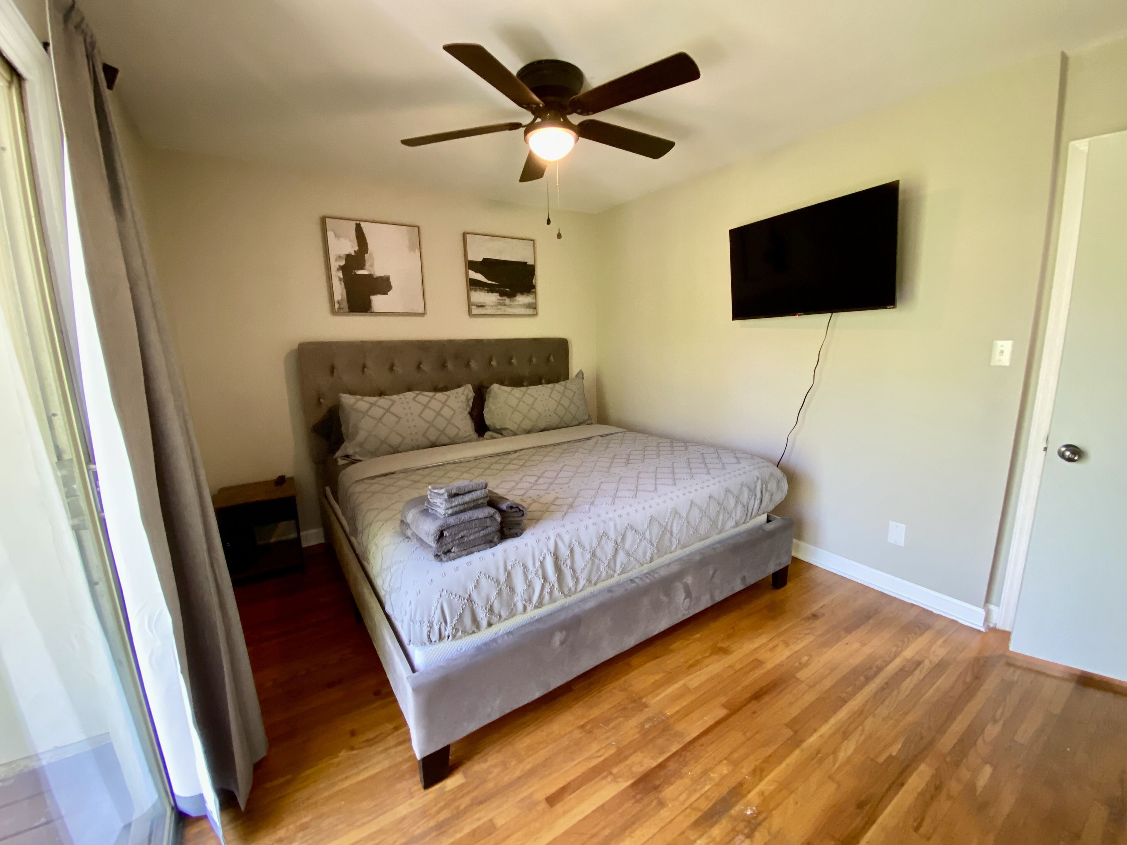 Un dormitorio con una cama, ventilador de techo y televisor de pantalla plana montado en la pared.