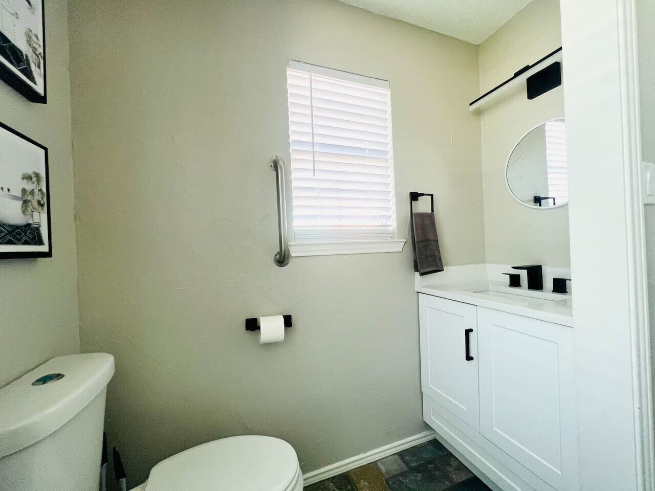 Un baño con inodoro, lavamanos, espejo y ventana con persianas.