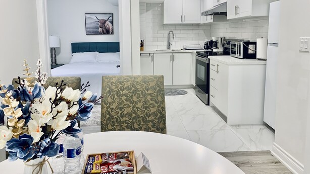 Ein modernes Hotelzimmer mit Bett, einer kleinen Küchenzeile und einem Essbereich mit Tisch und Stühlen.