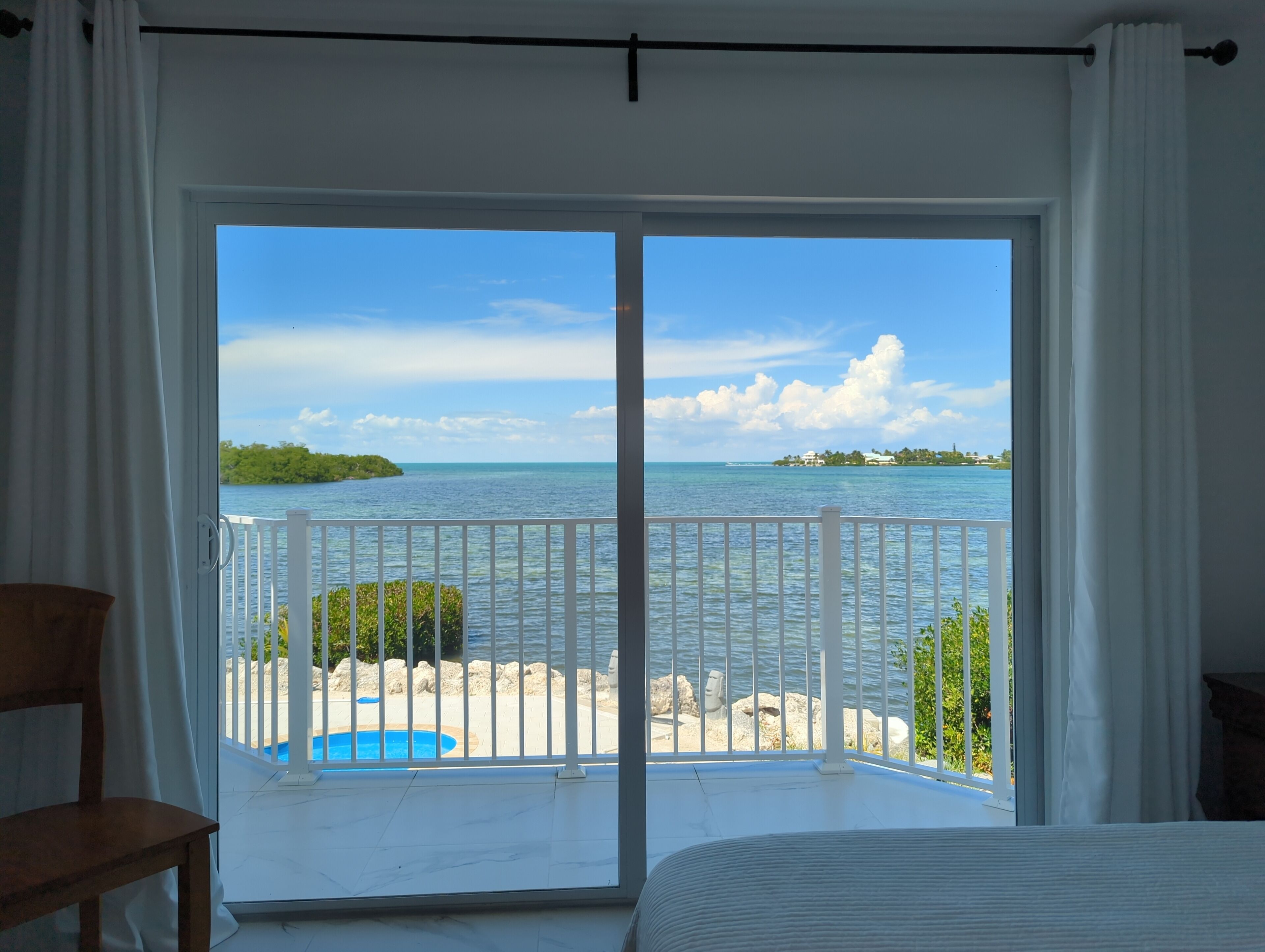 Une pièce dotée d’une grande porte-fenêtre coulissante donnant sur un balcon avec vue sur la mer et une île lointaine.