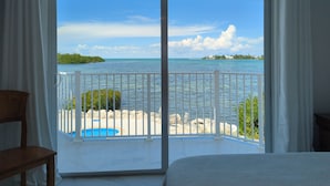 Een kamer met een grote schuifglazen deur die uitkomt op een balkon met uitzicht op zee en een eiland in de verte.