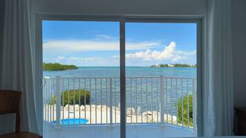 Une pièce dotée d’une grande porte-fenêtre coulissante donnant sur un balcon avec vue sur la mer et une île lointaine.