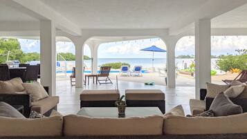 A covered outdoor seating area with a view of the sea, featuring lounge chairs, a table, and a grill.