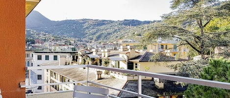 Un balcón con una mesa dispuesta para el té, con vistas a un pueblo en la ladera y una montaña al fondo.