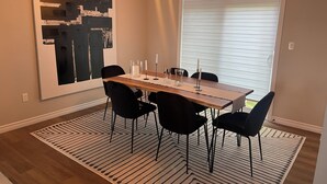 A dining area with a wooden table, black chairs, a patterned rug, and a large abstract painting on the wall. - Modern Townhouse, 5 Mins From all Amenities. (Guelph)