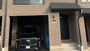 A modern two-story residential building with a garage entrance, a black car parked inside, and a number '3' sign on the door. - Modern Townhouse, 5 Mins From all Amenities. (Guelph)