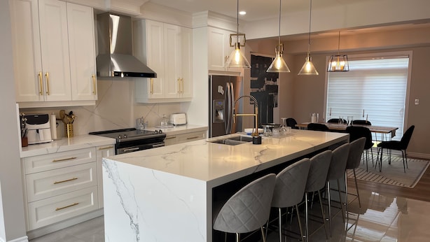 A modern kitchen with white cabinetry, a large island with bar stools, stainless steel appliances, and pendant lighting. - Modern Townhouse, 5 Mins From all Amenities. (Guelph)