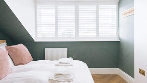 A bedroom with a bed, pillows, a radiator, a window, and a wall-mounted light fixture. - Sleek 1BD Flat 5 Mins From City Centre - Brighton (Brighton)