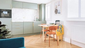 A modern kitchen with light green cabinets, a marble backsplash, and a dining area with a wooden table and orange chairs. - Sleek 1BD Flat 5 Mins From City Centre - Brighton (Brighton)