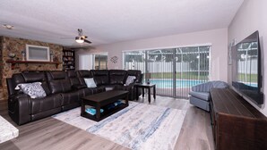 A living room with a leather sofa, a coffee table, a TV, and a pool view.