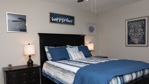 A bedroom with a dark wooden bed, blue bedding, two bedside tables with lamps, and wall art.