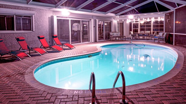 A swimming pool with red lounge chairs and a covered patio area.