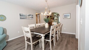 A dining area with a dark wooden table and white chairs, a chandelier, and a view of a cityscape through a doorway.