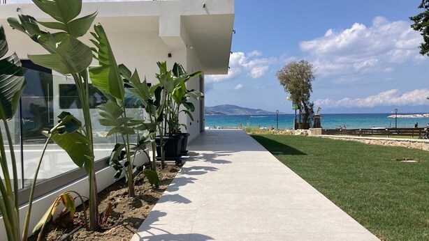 Ein modernes Gebäude mit einem Betonweg, der zu einer Rasenfläche und dem Blick auf das Meer führt.